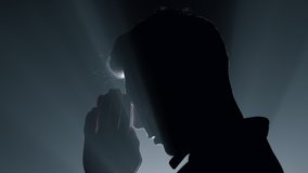 Silhouette of young man praying in spotlights background. Side view religious male person whispering prayer in darkness. Believer human folding hands for prayer indoors. 