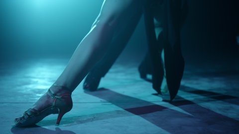 Closeup of couple legs doing latin dance steps on floor. Unknown professional partners feet dancing indoors. Unrecognizable dancers performing in dark background.