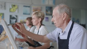 High angle view of cheerful senior friends painting on canvas. Senior woman smiling while drawing with the group. Seniors Attending Painting Class Together. Senior men having fun painting in art class - Powered by Shutterstock - Get 15% off with code: PIKWIZARD15