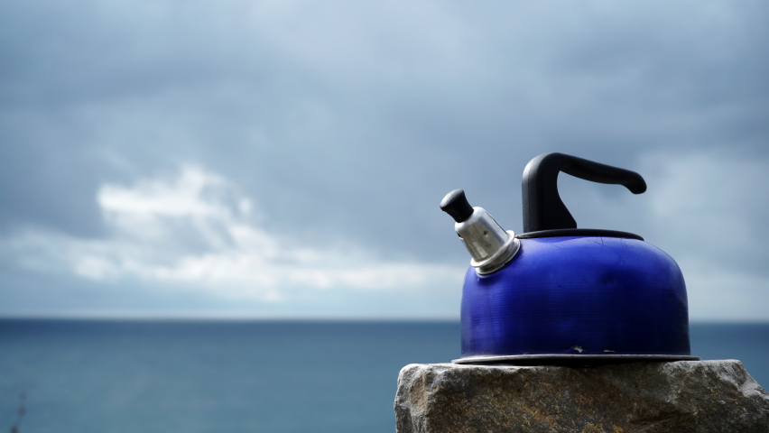 Clouds moving over sea and kettle camp equipment on sea shore. Travel, camping on nature.
