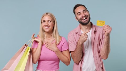 Young couple two friends family in pink clothes together man hold in hand credit bank card womanholding package bags with purchases isolated on pastel plain light blue color background studio portrait