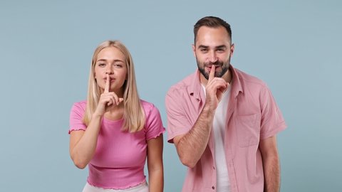 Secret young couple two friend family bearded man woman in pink clothes together say hush be quiet with finger on lips shhh gesture isolated on pastel plain light blue color background studio portrait