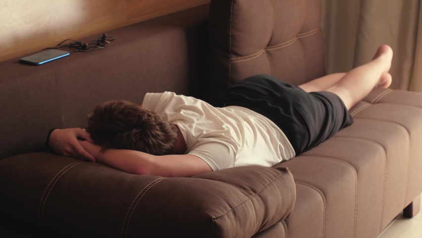 Exhausted overworked young unrecognizable man lies on the couch in the afternoon. Concept after party, tired, overworked person, hard day, lack of energy | Shutterstock HD Video #1076749397