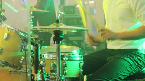 The drums and cymbals during playing. Drum set, drum kit in dark, drummer plays a concert. The drummer hits the wet drum. Young man playing drums on stage. Concert. Neon light