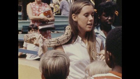 1970s: zookeeper walking with monkey on rail around petting zoo, zookeeper with snake around neck at petting zoo, people at petting zoo feeding furry cows