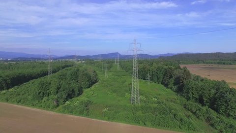 AERIAL: Flying pass transmission towers and high voltage power lines across the agricultural wheat fields and forests