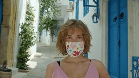 a portrait of a attractive woman in a designer protective face mask with a floral print looking at the camera. a tourist visiting Greece, Cyprus, Spain and Italy during corona pandemia. a stylish way