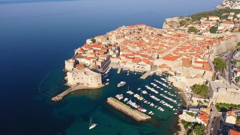 Aerial drone footage of the famous Dubrovnik medieval old town and harbor with its fortified walls and tower by the Adriatic sea in Croatia on a sunny summer