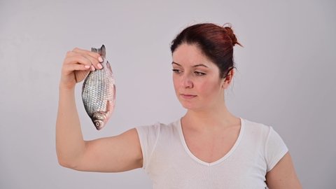 Caucasian woman is horrified by the smell of fish and pinches her nose with a clothespin on a white background.