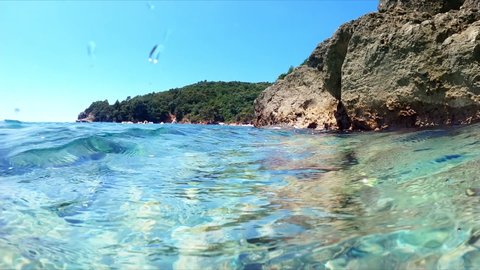 Slow-motion half underwater video at the border of air and water. Beautiful rocky beach on the Adriatic Sea in Montenegro.