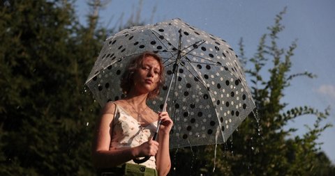 Teenage beautiful girl with an umbrella in the pouring rain and sunshine. Vacation concepts. Slow motion. Cinematic look