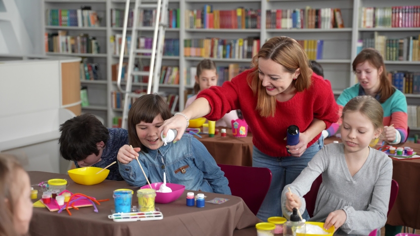 Positive female teacher squeezing shaving foam for slime into bowls of joyful kids with autism. Inclusive education for children with special needs | Shutterstock HD Video #1076780702