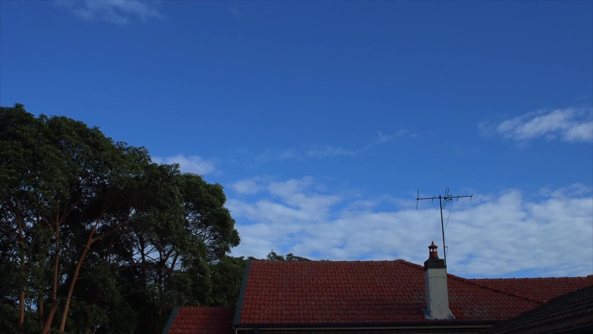 time lapse Fast moving clouds against a nice blue sky with a red roof suburban house and tree in the foreground Sydney NSW Australia