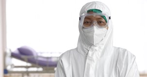 Video portrait shot of medical person wearing PPE, Personal Protective Equipment, clothes standing and looking to camera in hospital.
