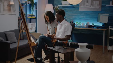 Black creative people using laptop computer for drawing design of vase at studio. African american man and woman working on modern masterpiece with white canvas and easel. Artistic couple