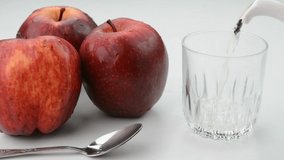 Pouring apple cider vinegar in a glass cup with red apples in the background