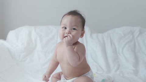 portrait of asian baby infant 6 months old naked after bathing covered with white towel. happy innocence baby kid smile happily. sucking hand age baby portrait copy space provided. smiling baby laugh.