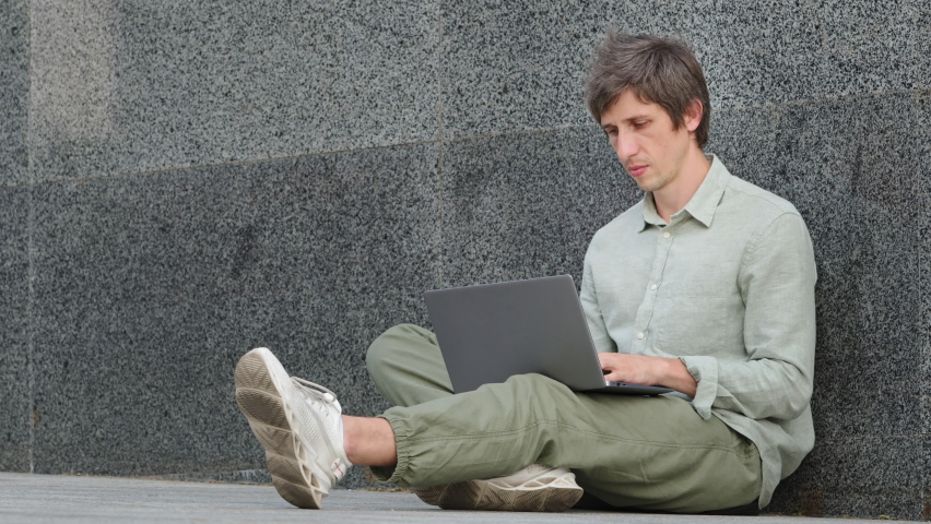 Sad apathetic depressed young adult man sitting outdoors with laptop feeling angry, annoyed, due to low battery or no internet. Guy received bad news, email, scholarship denied, resignation message Royalty-Free Stock Footage #1076817839