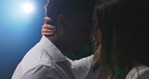 Sensual dance of two partners, close-up on faces being very close to each other, couple is looking into eyes, focused on each other, twilight, in the background bright single light, blue glow