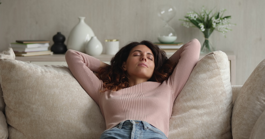 Peaceful happy attractive latin female homeowner relaxing on comfortable sofa, breathing fresh air, daydreaming napping enjoying lazy carefree weekend pastime alone in living room, recreation concept. Royalty-Free Stock Footage #1076831039