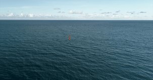 A kite surfer rides on a hydrofoil board far in the ocean. View from a drone to a kitesurfer. A large orange kite. The athlete rides at high speed over the surface of the water. Far from the coast