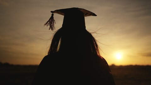 Graduates wear a black hat to stand on top of hill congratulations on graduation at silhouette sunset time	