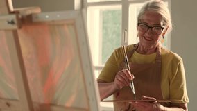 Senior Artist, Art Workshop, Sun Rays, Painting Woman. Happy senior woman artist paints a picture on canvas - Powered by Shutterstock - Get 15% off with code: PIKWIZARD15