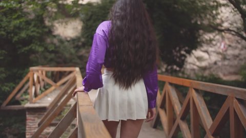Girl With Short White Dress and Violet Top Walking on Wooden Bridge in Botanical Garden in Slow Motion