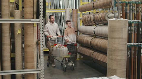 Slowmo shot of family with shopping cart looking at rolls of linoleum at home improvement store