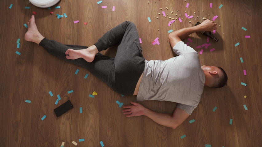 A man sleeps after a party on the floor in an apartment while cleaning a robot vacuum cleaner. Smart House. Hangover after drinking at the party. Room cleaning Royalty-Free Stock Footage #1076845739