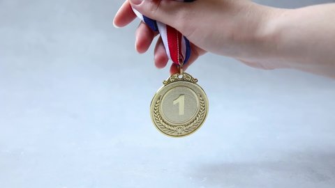 Hand holding winner or champion gold trophy medal on concrete stone grey background. Victory first place of competition. Winning or success concept.