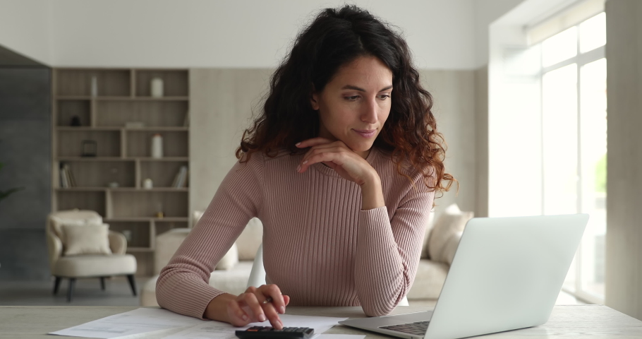 Concentrated young happy hispanic woman involved in domestic financial paperwork, calculating utility bills, managing household budget, making payment online in computer e-banking application. Royalty-Free Stock Footage #1076855741