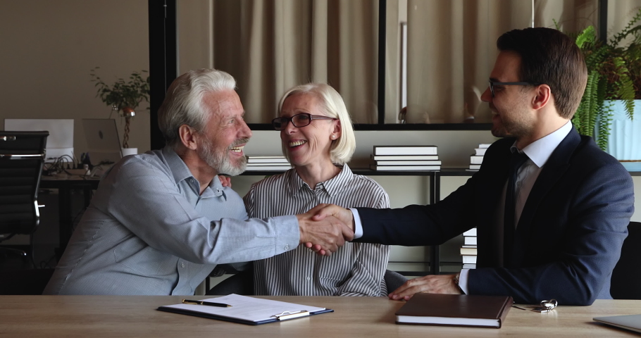 Old 50s couple discuss flat purchase with professional real estate agent at meeting in office, spouses sign agreement, get keys from own accommodation, shake hands realtor celebrate deal looking happy | Shutterstock HD Video #1076855753