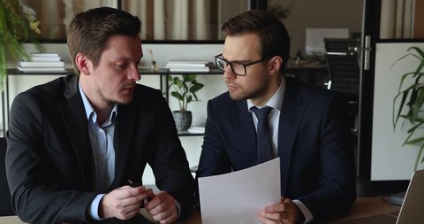 Two businessmen in formal suits meet in office for contract discussion. Client manager negotiate agreement terms conditions, analyzing further partnership, consider business plan, do paperwork concept