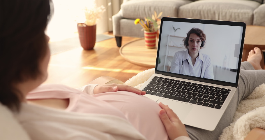 Rear shoulder view young pregnant woman holding computer video call conversation with female obstetrician gynecologist, discussing pregnancy diagnostic screening results, medical help concept. Royalty-Free Stock Footage #1076855858