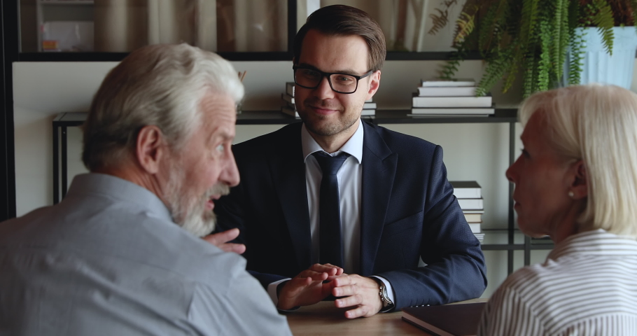 Happy older spouses receive professional consultation from insurer during formal meeting in office. Bank employee provide help informing to elderly clients. Mortgage, loan, insurance services concept Royalty-Free Stock Footage #1076855894
