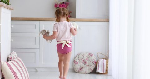 rear view of toddler baby girl running away with toys at the living room at home