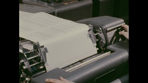 1970s: Woman pulls printed out paper from dot matrix printer. Man sits at word process, dot matrix printer. Server machine spins reel tapes.