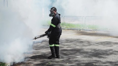 Professional person with equipment using a fogging machine with insecticide to eliminate mosquitos as aedes aegypti and chicungunya in an outdoors environment during the day under the sun
