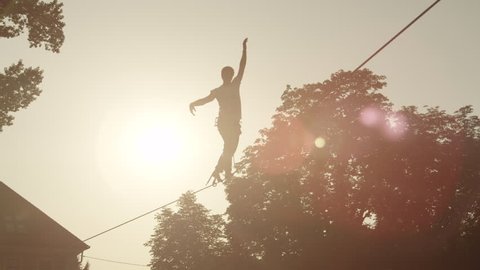 SLOW MOTION: Young man balacing on slackline between the houses in big city at beautiful sunset