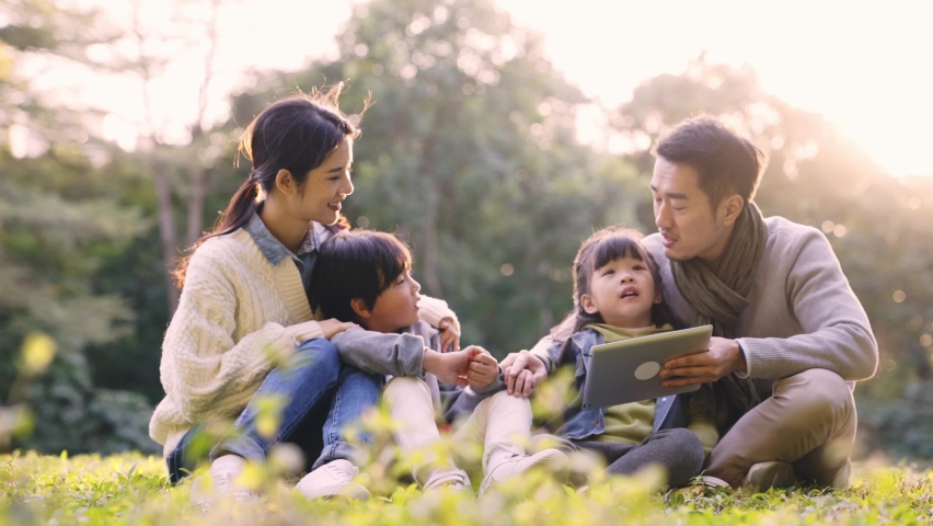 asian family with two children sitting on grass talking relaxing outdoors on in park at sunset Royalty-Free Stock Footage #1076862956