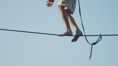 CLOSE UP of the mans feet walking on the slackline