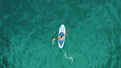 Drone footage of a tourist paddling within the ocean. Man uses SUP board and paddle in turquoise sea water. High quality 4k footage
