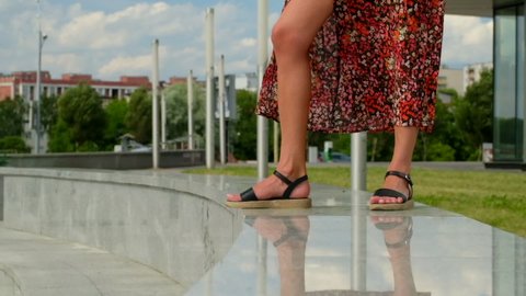 Super slow motion of female legs in sandals and dress fluttering in the wind