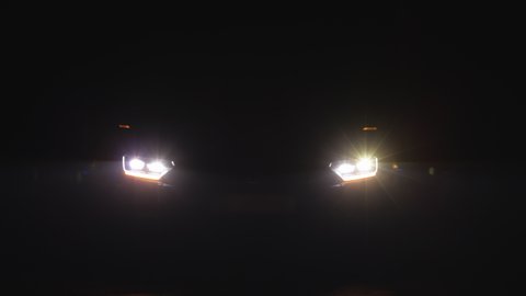 Car headlight blinking in Dark. Sports car Headlight. Shot of blinking headlights in car. LED Light New Luxury Car. Emergency light signal, warning sign. Nobody around to help.