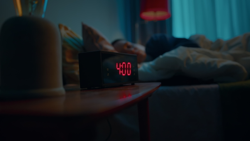 Young sleeping woman wakes up early in morning to disable activated digital alarm clock on bedside table. Doing this she turns away to sleep in covered up in soft blanket. Slow motion cinematic shot Royalty-Free Stock Footage #1076870705
