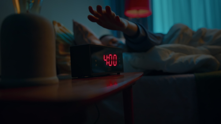 Young sleeping woman wakes up early in morning to disable activated digital alarm clock on bedside table. Doing this she turns away to sleep in covered up in soft blanket. Slow motion cinematic shot | Shutterstock HD Video #1076870705