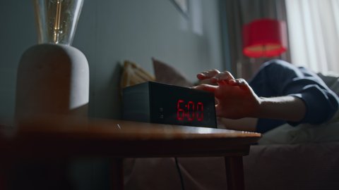 Young woman sleeping in bed at home wakes up to digital alarm clock on bedside table to disable it. She stretches before getting out of bed to energize her body in morning. Slow motion cinematic shot