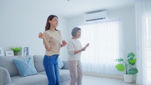 Asian funny senior old mom and daughter dance together in living room. Attractive beautiful woman and mature grandma feel happy to spend leisure time at home, enjoy listen to music on weekend in house