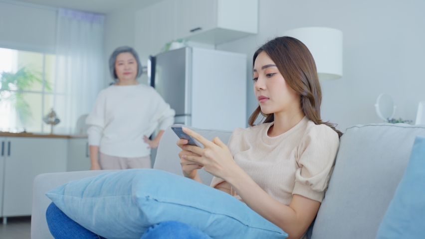 Asian angry senior mature woman shouting at stubborn fussy daughter. Young female sit on sofa use mobile phone chat, disobedient rebellious and ignore annoyed mother. Family problem in house concept. Royalty-Free Stock Footage #1076872841